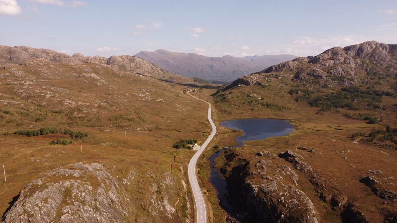Aerial shot of a picturesque road weaving through the rocky landscapes of the Scottish Highlands.